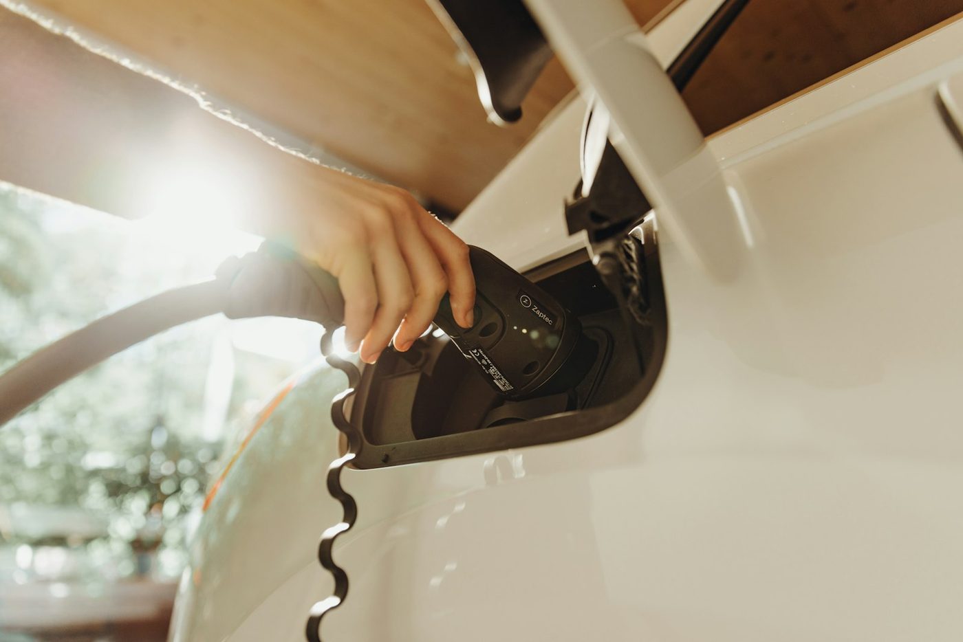 Driver plugging a charging cable into an electric car at golden hour